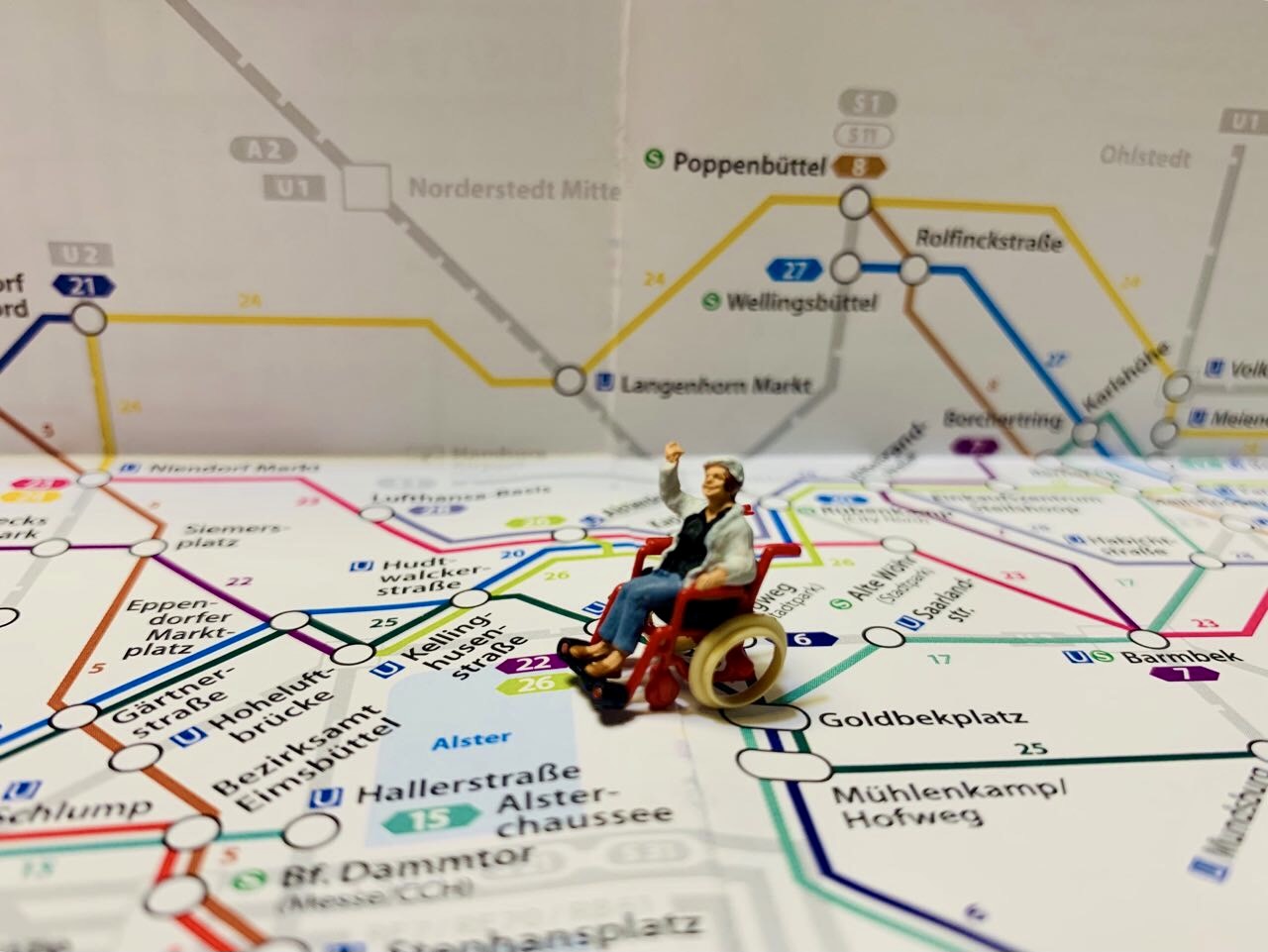 Ein Plan des Hamburger U- und S-Bahn Netzes. Darauf eine kleine Figur. Eine winkende Frau im Rollstuhl